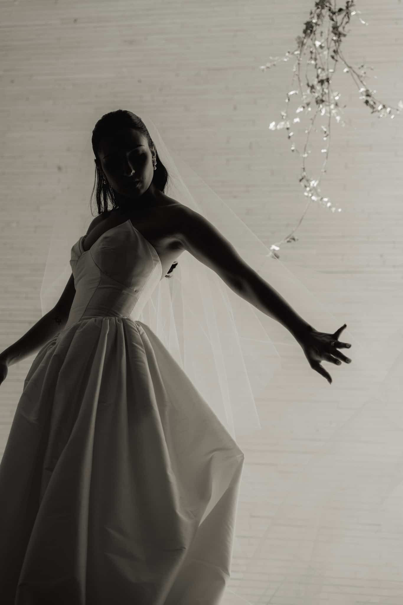 Silhouette of a bride dancing with her arms out against a bright wall