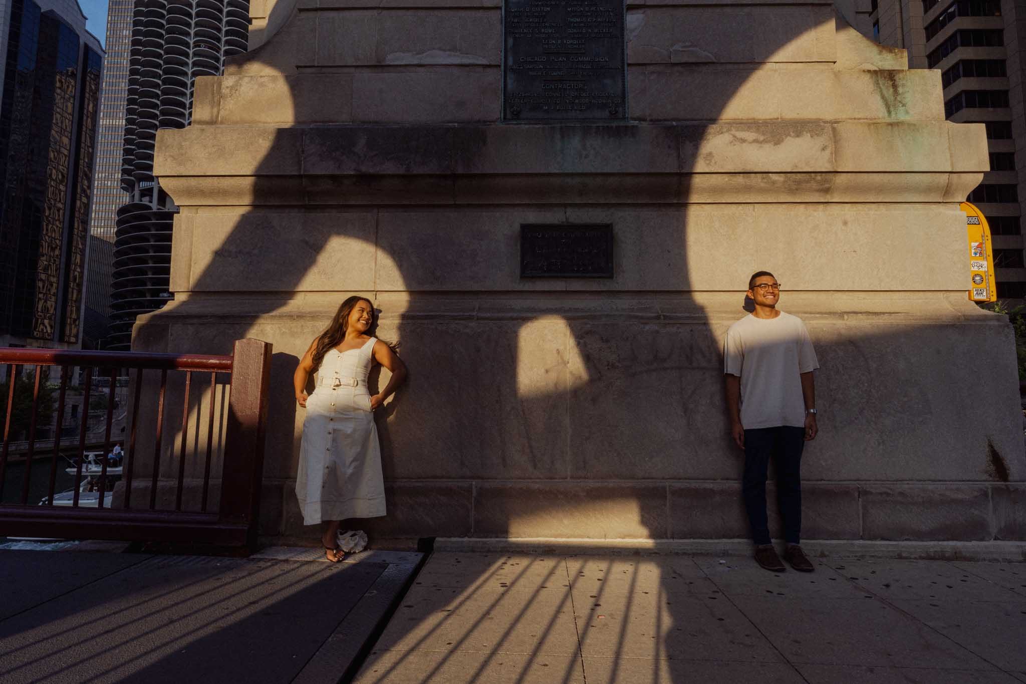 Alexis and Jason in pools of sunlight against a Chicago River bridge house