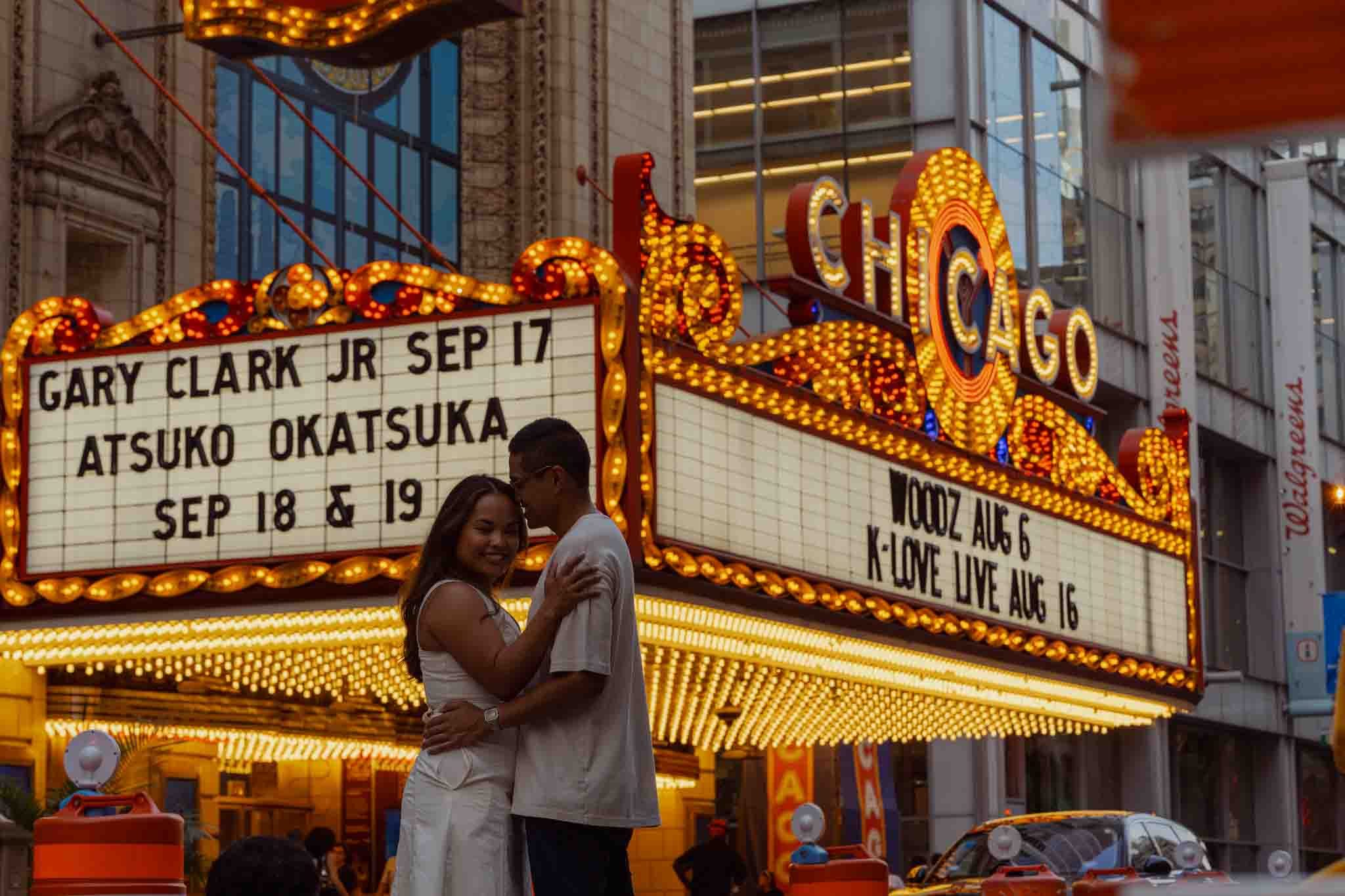 Alexis and Jason embracing under the lit Chicago Theatre marquee