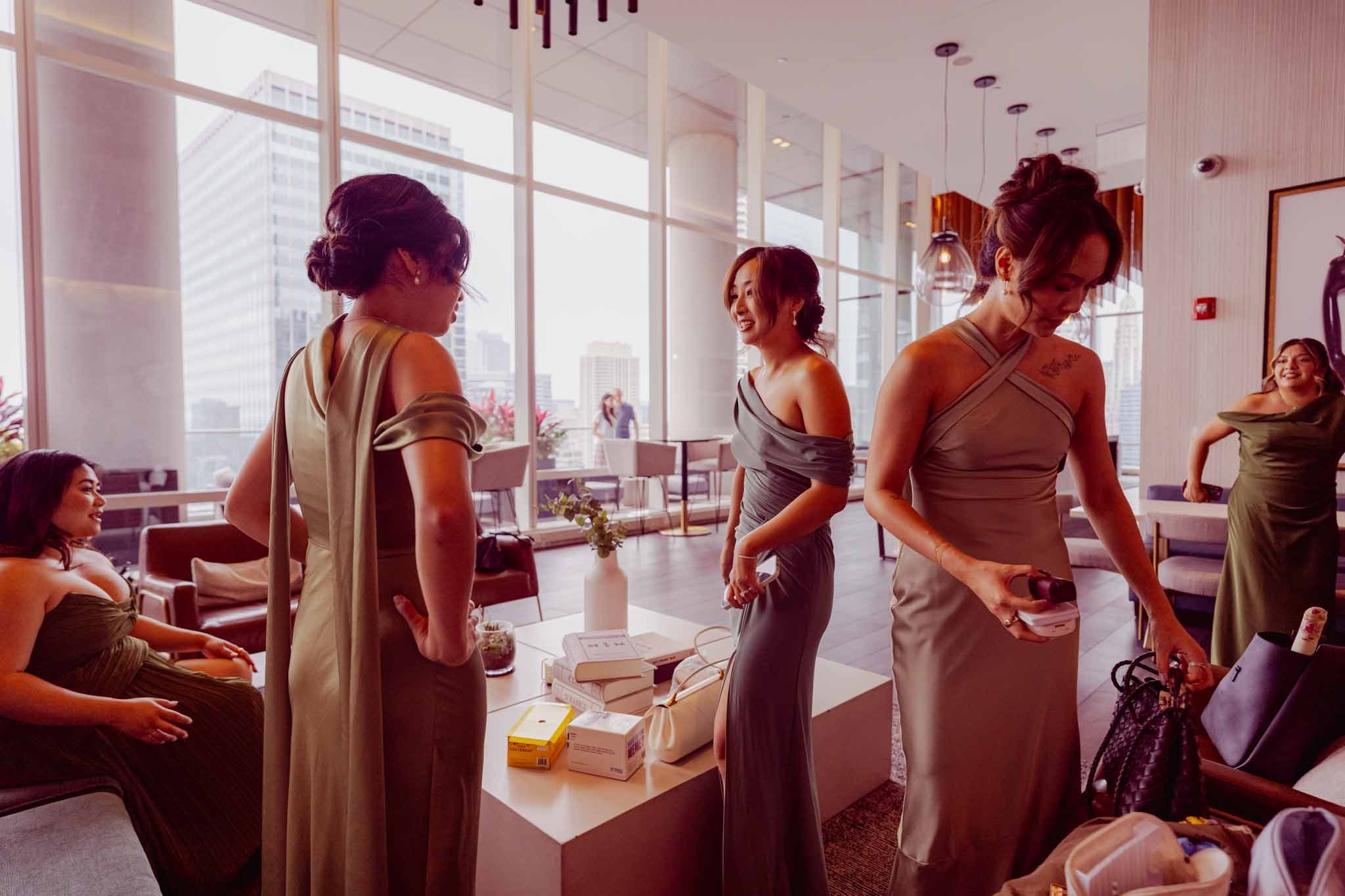 Bridesmaids in green and sage dresses getting ready in a bright Chicago high-rise lounge