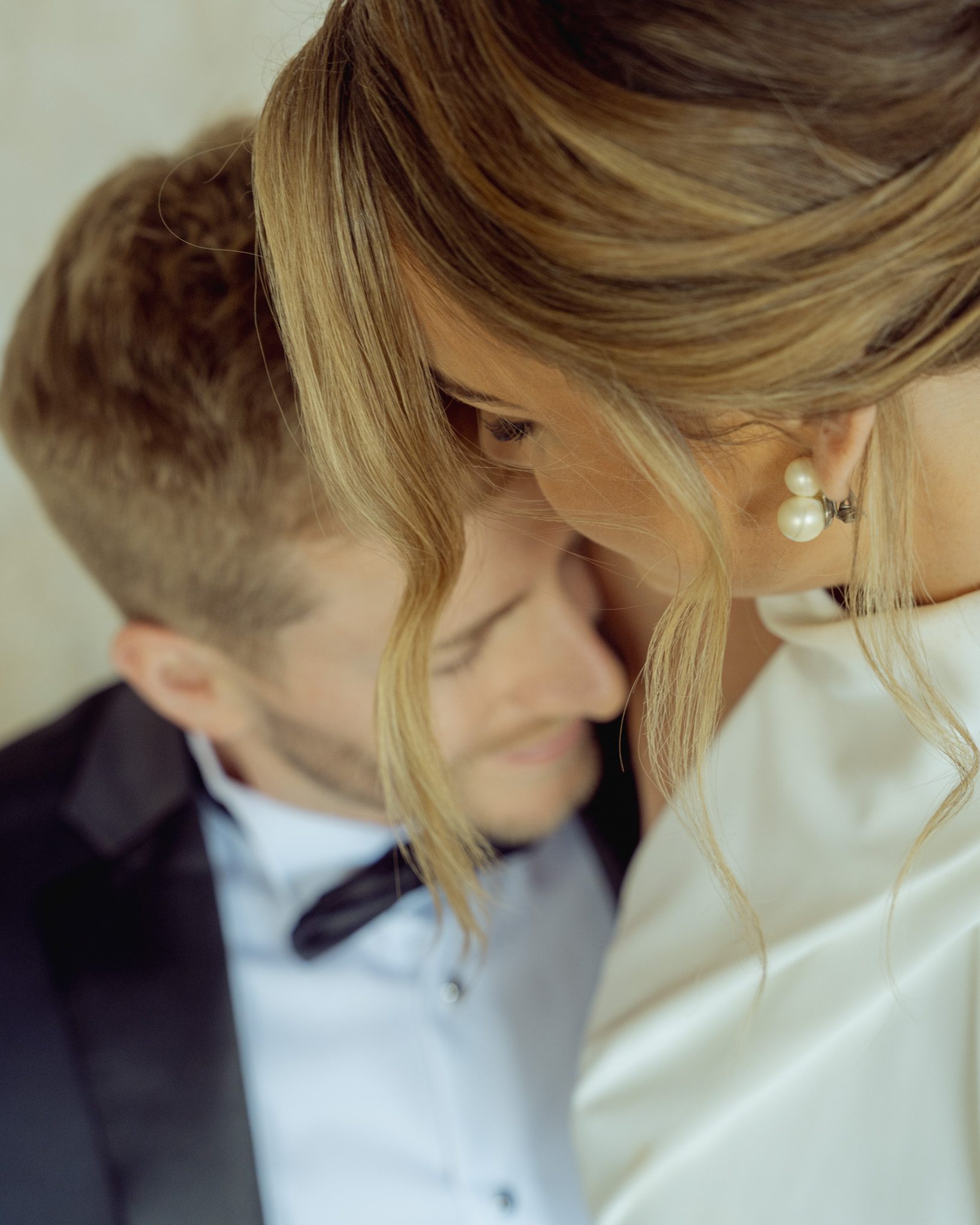 Close portrait of a bride resting her head against the groom's, pearl earring and loose hair