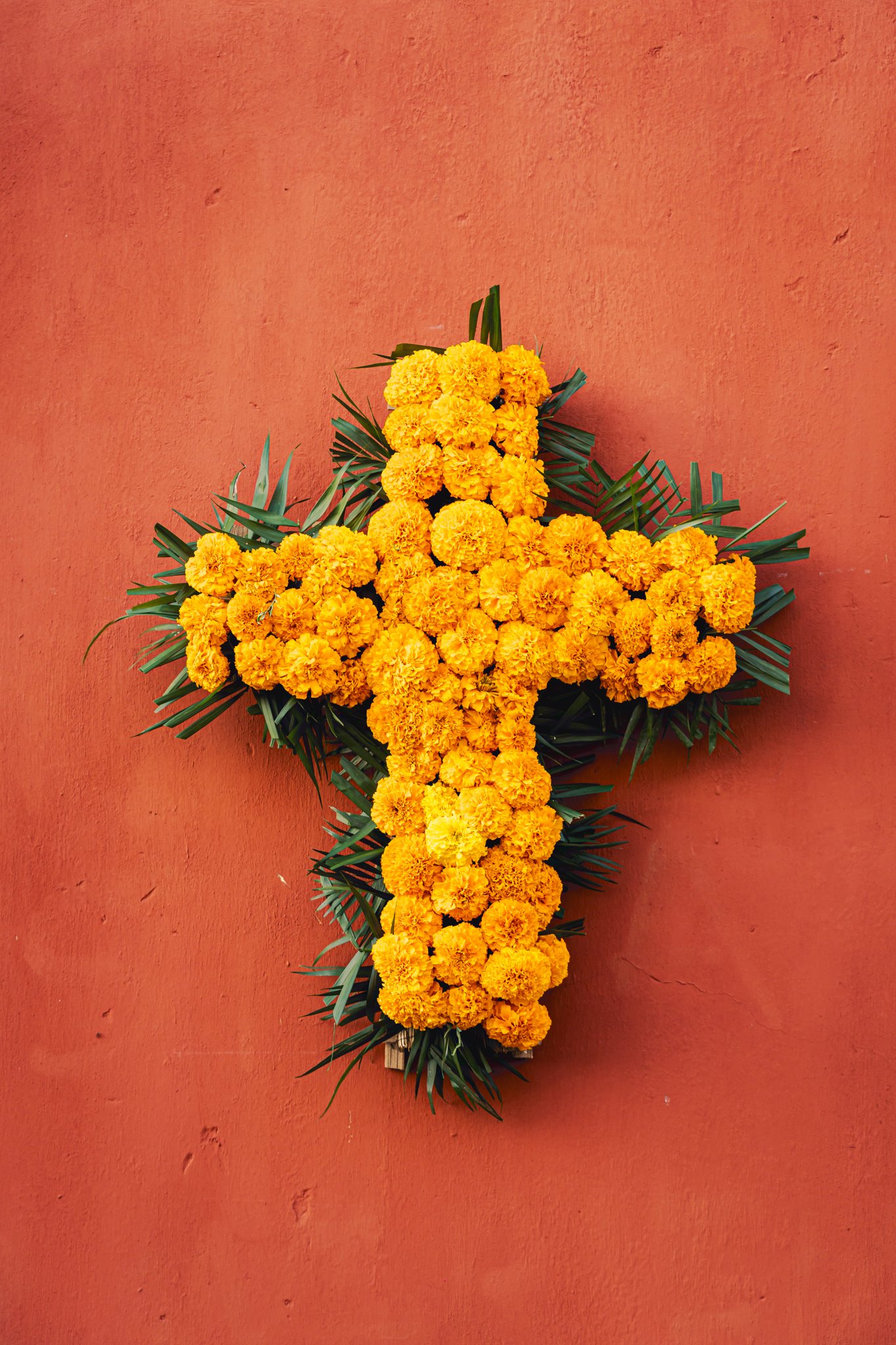 A cross made of marigolds on a terracotta wall