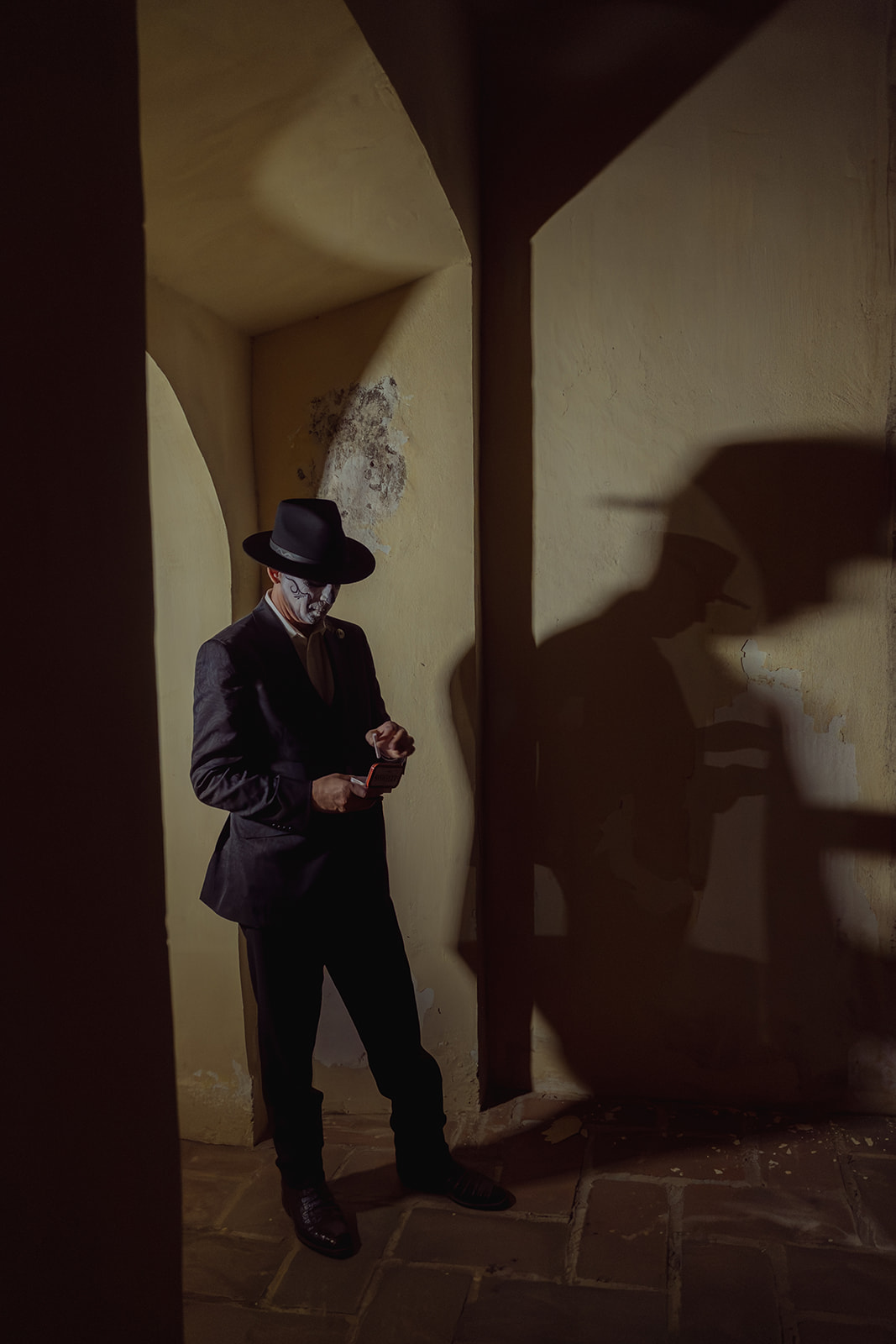 A catrín in a hat against a blank wall, his shadow cast large beside him