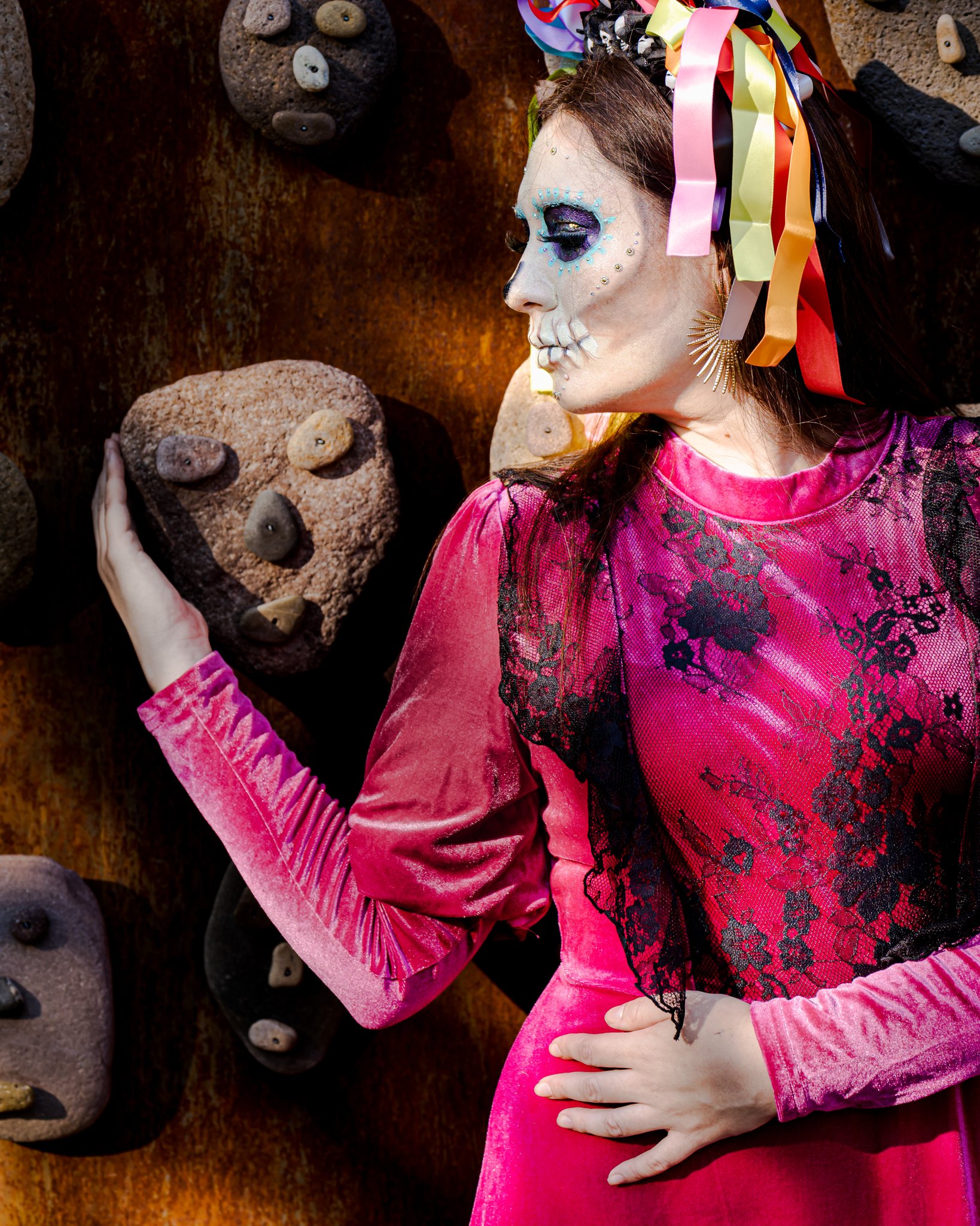 A catrina in profile resting her hand on a carved stone skull