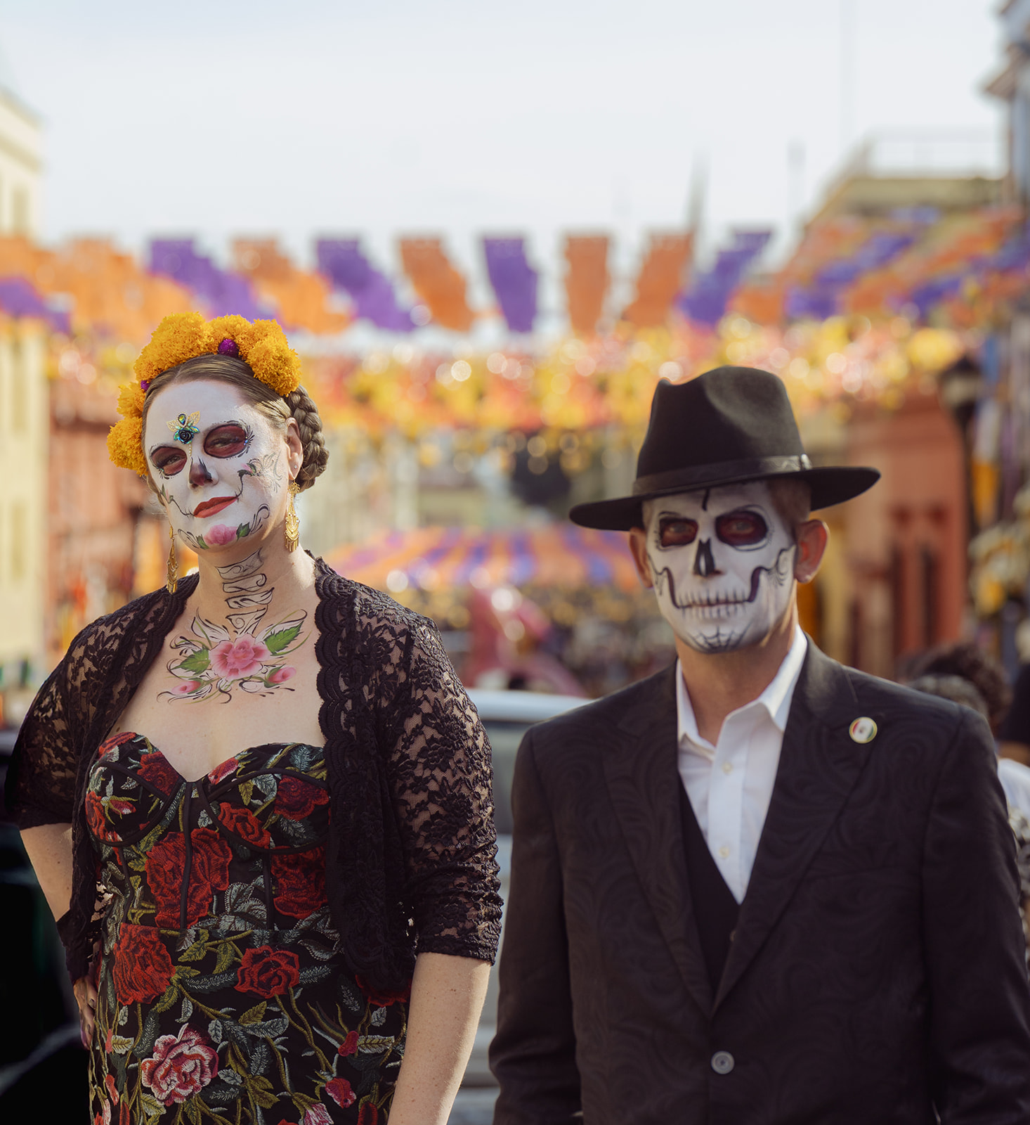 A couple painted as catrina and catrín under papel picado on a street in Oaxaca's Centro
