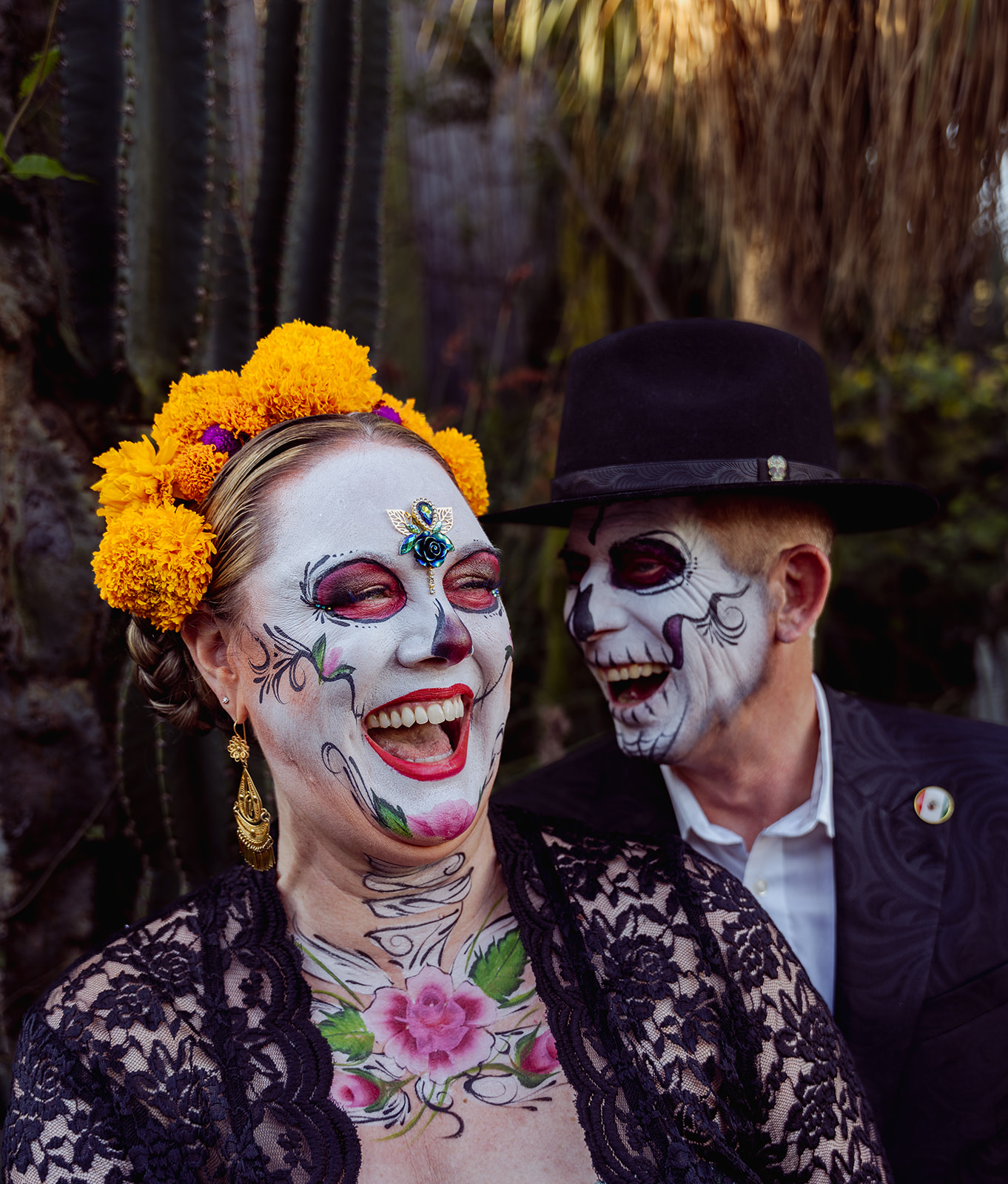 A catrina with a crown of marigolds laughing with her catrín among the cactus at Vives Verde