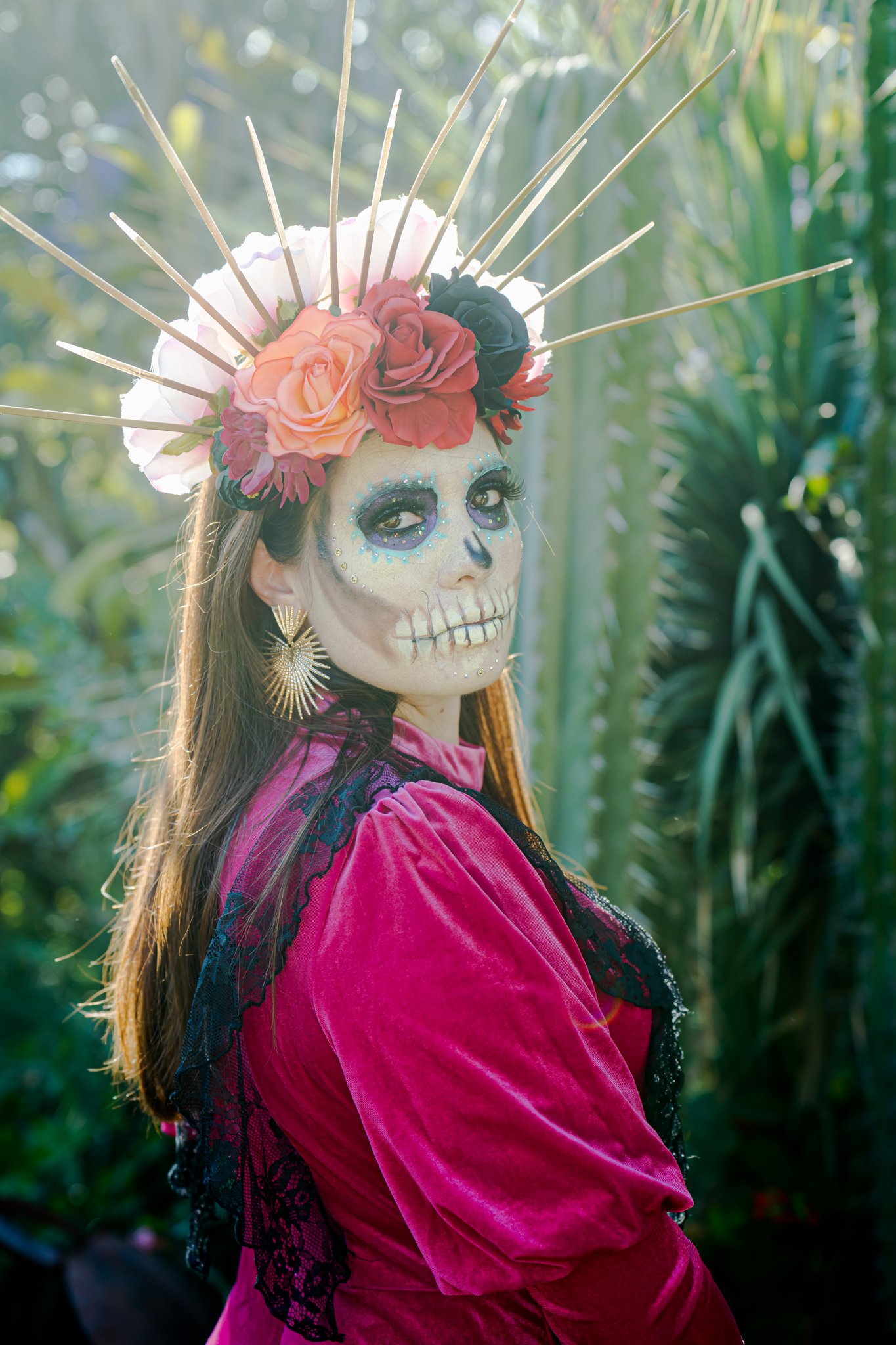 A catrina in a magenta velvet dress and a crown of roses among cactus in Oaxaca