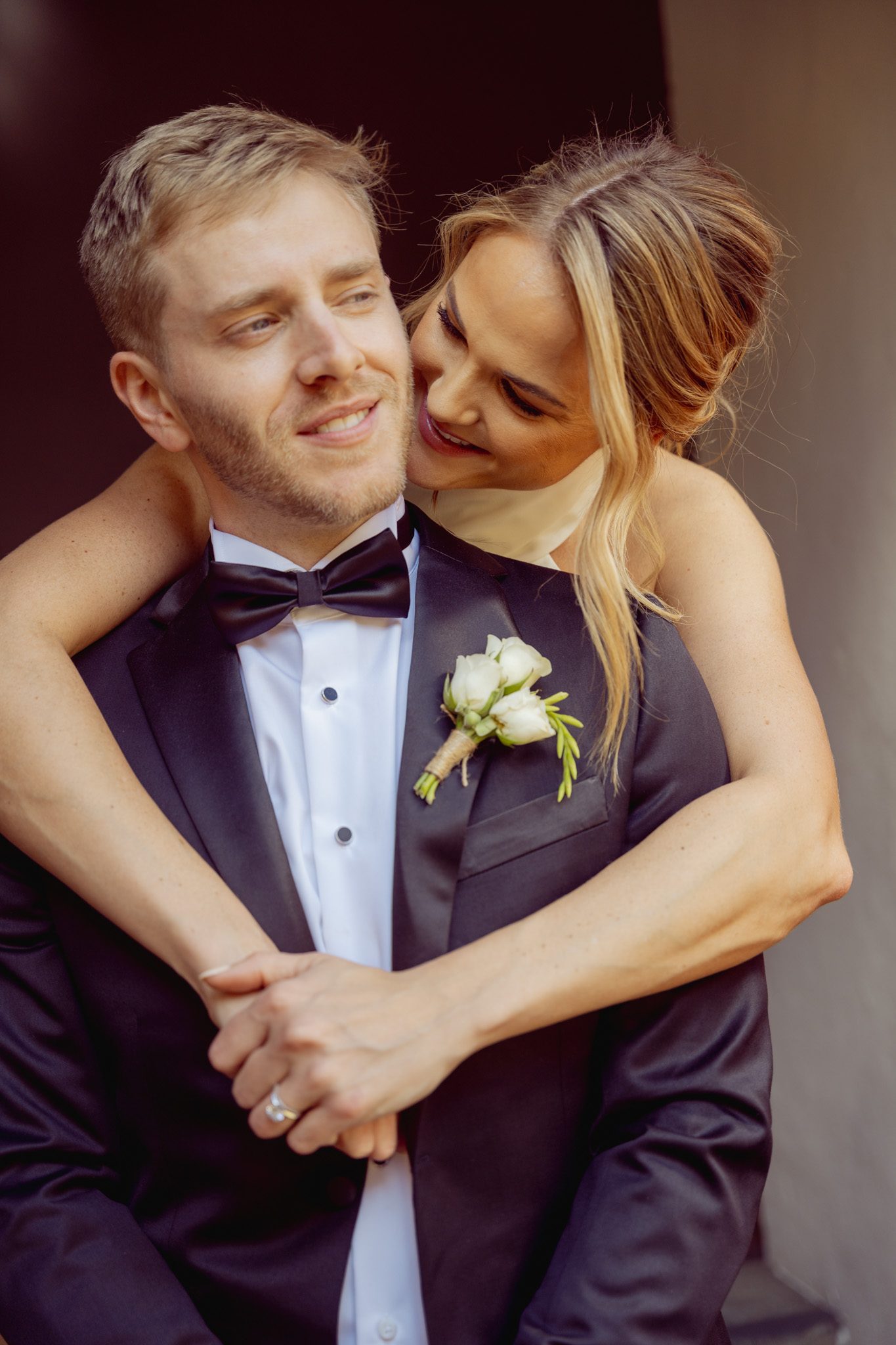 Bride wrapping her arms around the groom from behind, both smiling