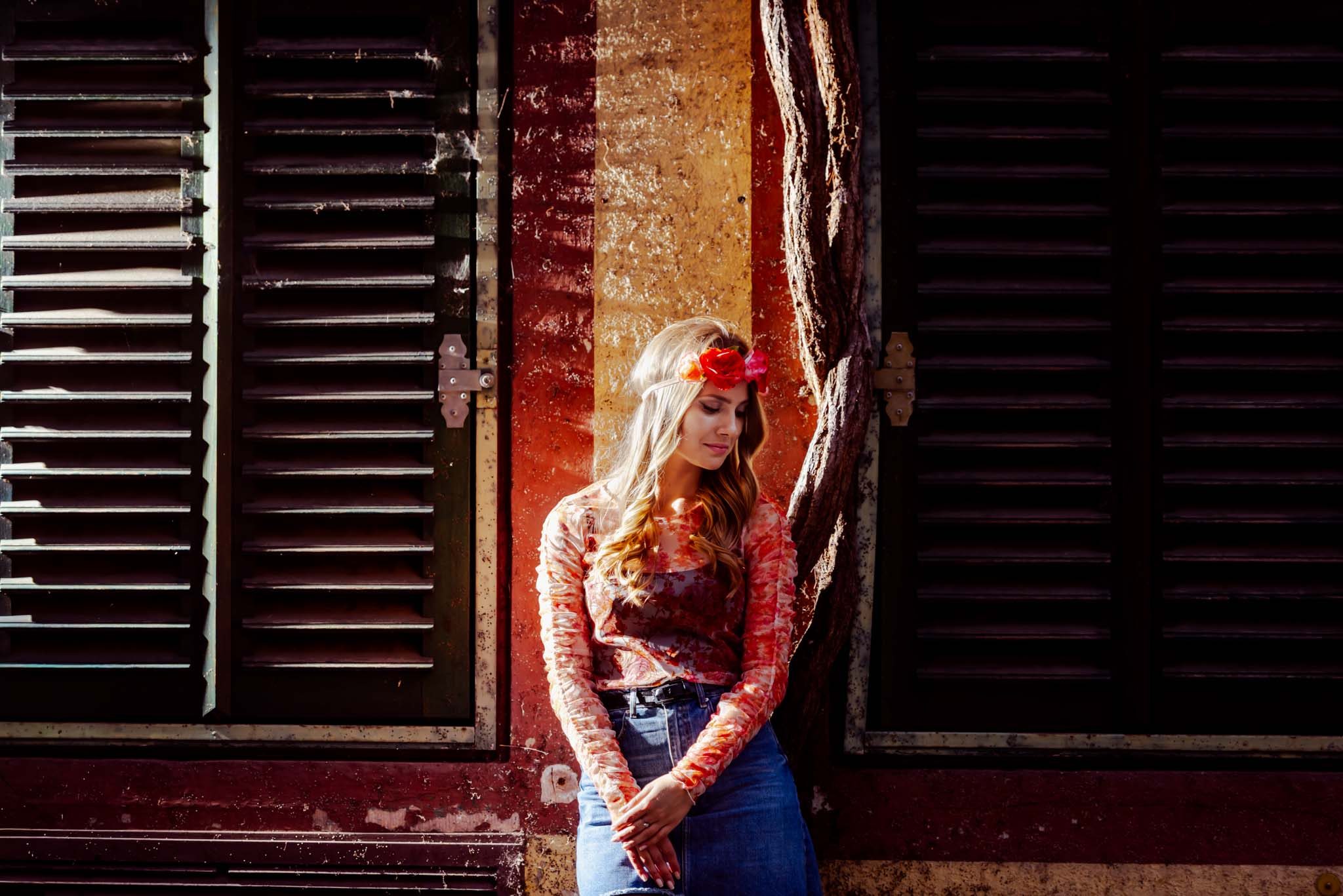 Portrait of a young woman leaning in a doorway between dark wooden shutters