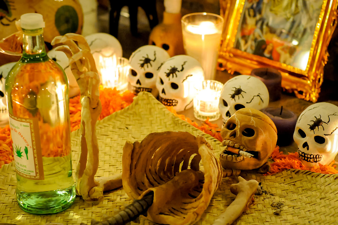 A candlelit ofrenda with skulls, marigolds, and a bottle of mezcal, Oaxaca