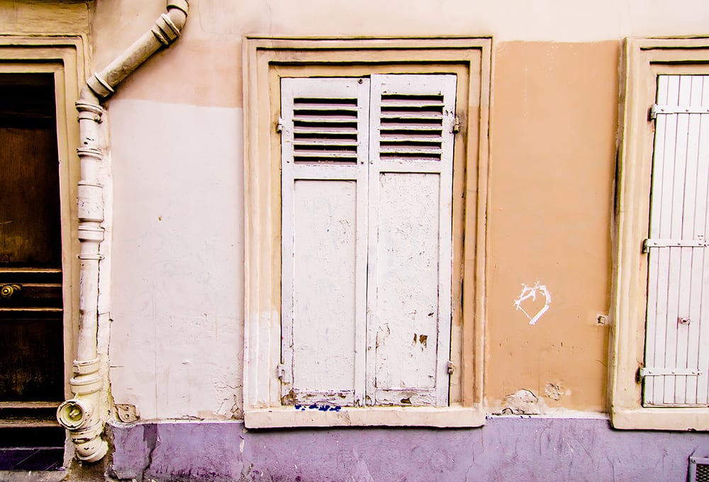 A small heart scratched into a plaster wall beside a white window shutter in Paris