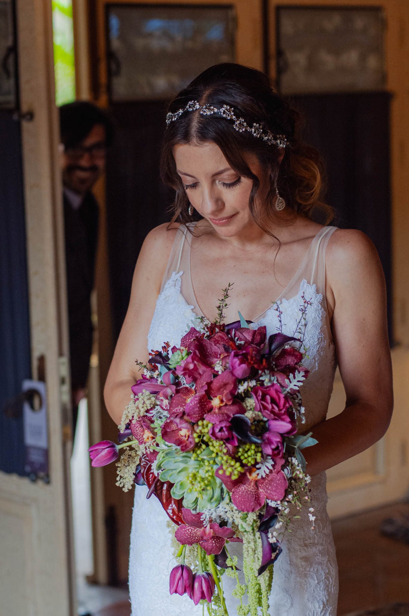 Bride looking down at her bouquet of magenta orchids in a doorway at Hotel Nena