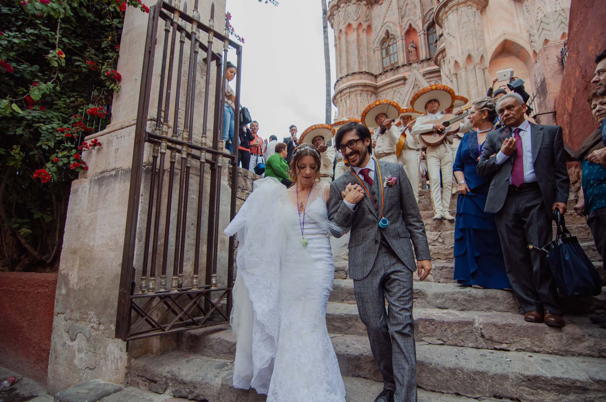 Bride and groom coming down the steps of La Parroquia arm in arm, mariachis and guests behind them