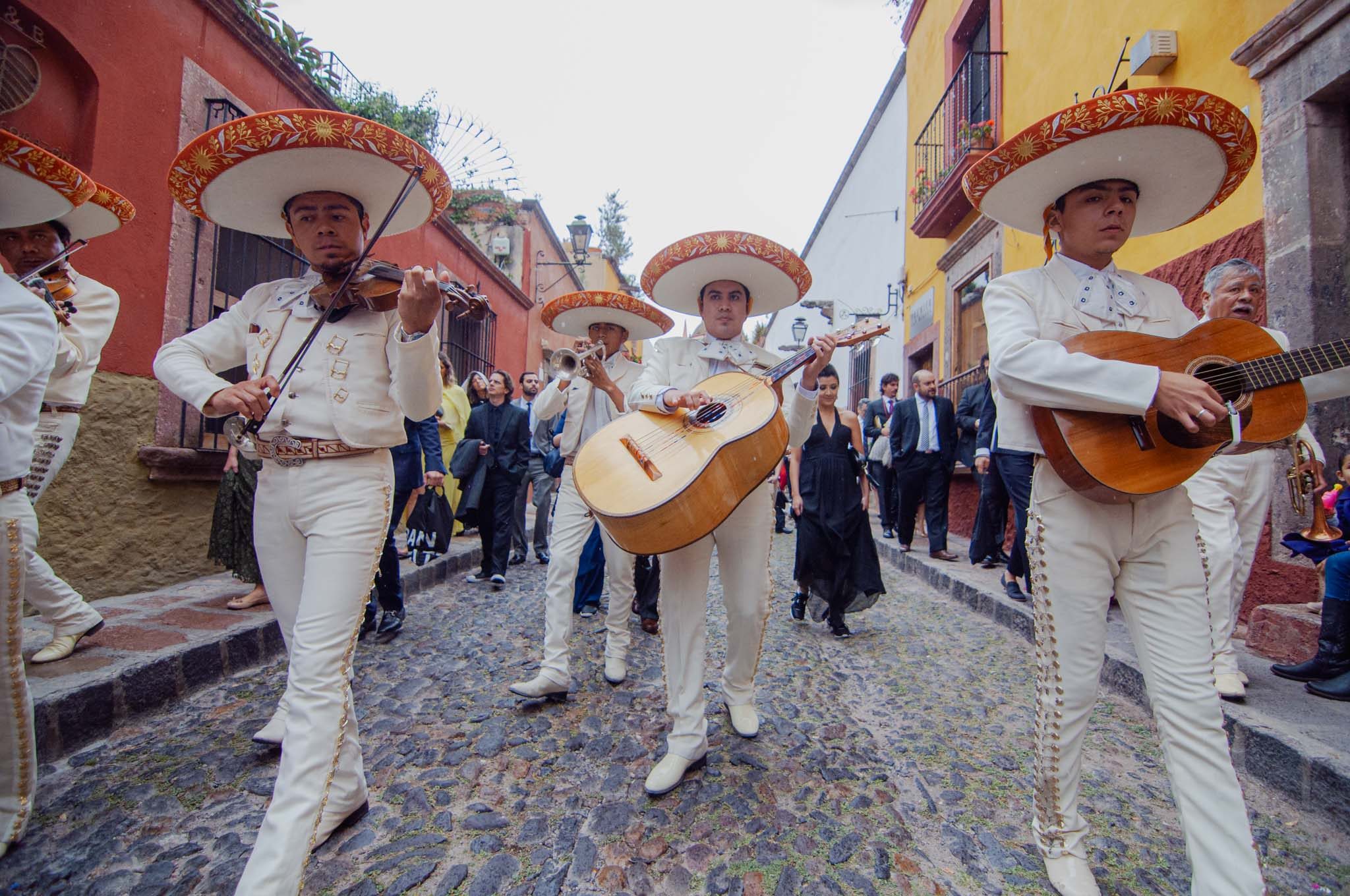 Mariachis leading the wedding callejoneada down a colorful San Miguel street