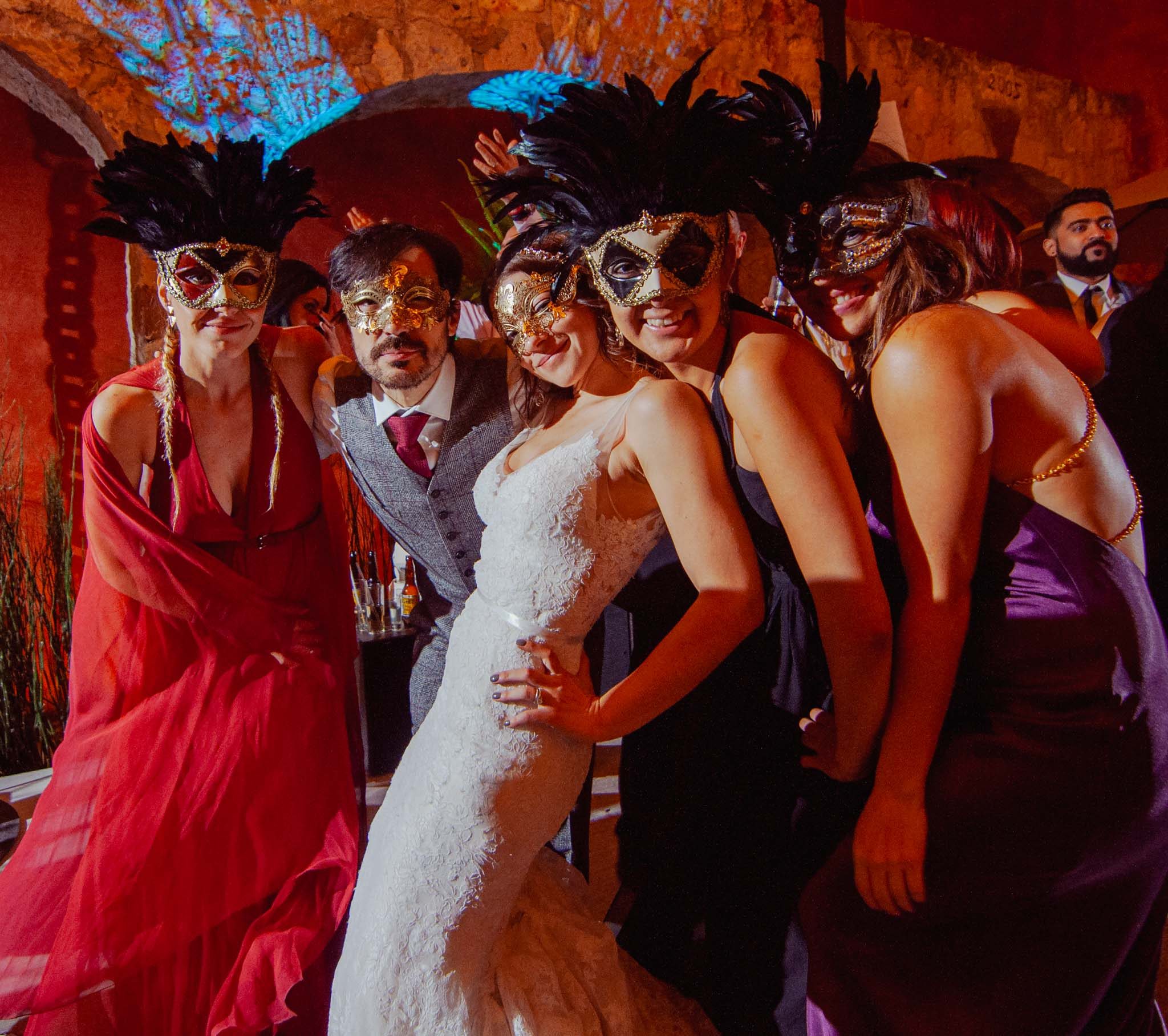 Bride, groom, and friends in feathered masquerade masks at the reception at Hotel Nena