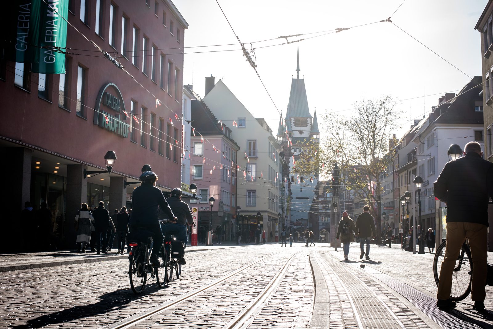 Cyclists on Kaiser-Joseph-Straße in low sun, with the Martinstor at the end of the street
