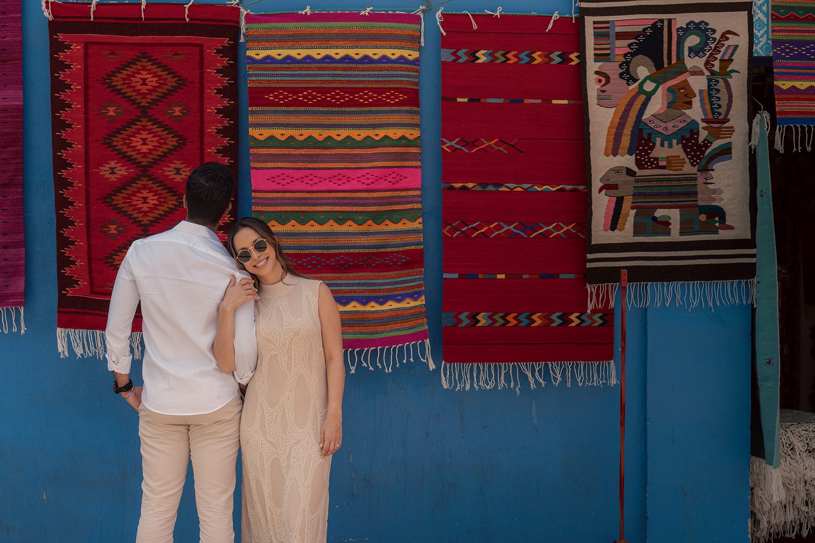 In front of handwoven rugs on a blue wall