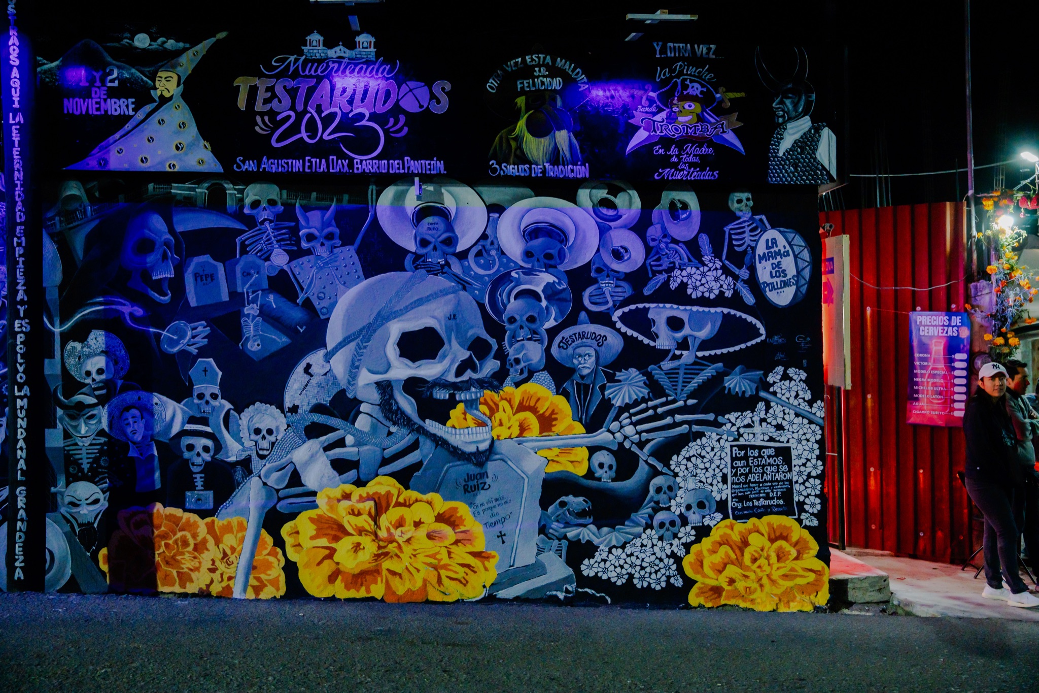 A blue skull mural lit at night, with painted marigolds