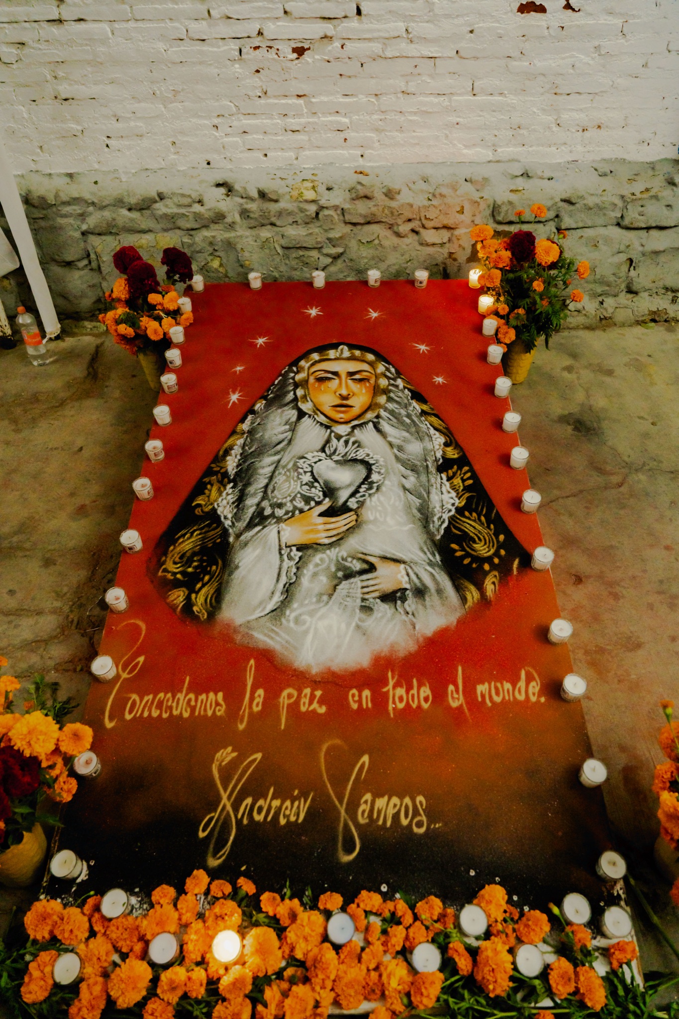 A Día de Muertos sand rug with an image of the Virgin, framed by marigolds and candles
