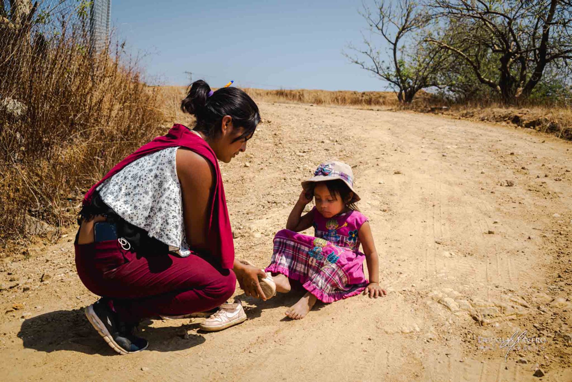A mother kneeling with her daughter on a dirt road